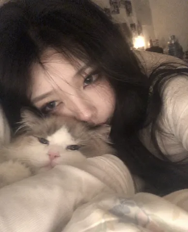 Close-up blurry snapshot of a dark-haired woman holding a cat under a quilt, with only her eyes visible.