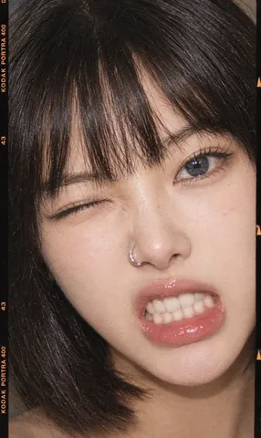 Extreme close-up of a young woman winking and baring teeth with a nose ring in grainy film style.