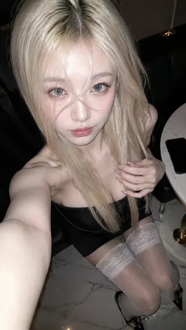 High-angle close-up selfie of a platinum blonde woman with clear round eyes looking up.