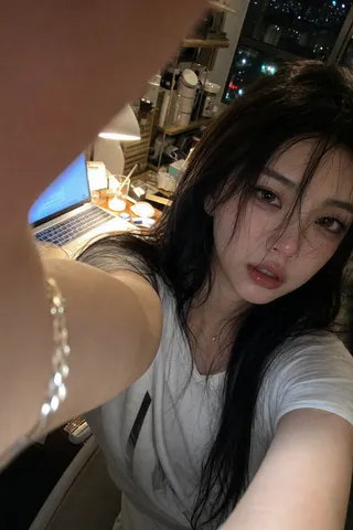 High-angle selfie of a woman in a dimly lit, cluttered room with a finger partially in frame