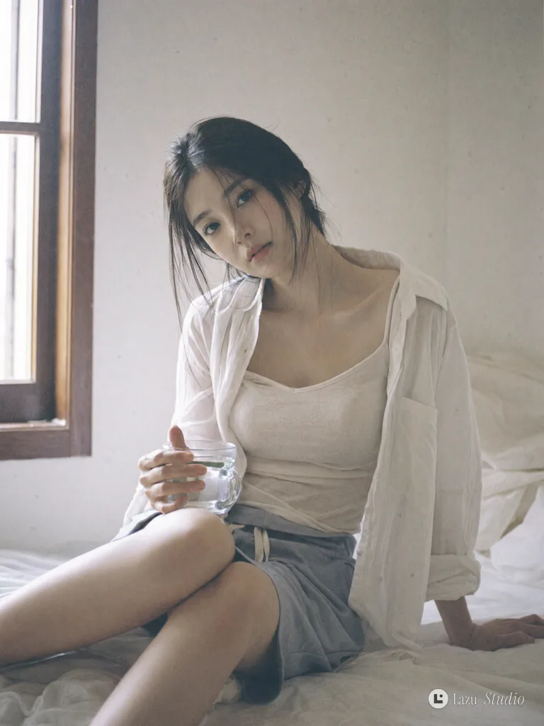 Woman in an open white shirt sitting quietly by a bright window holding a cup