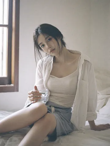 Woman in an open white shirt sitting quietly by a bright window holding a cup