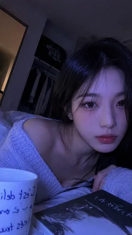 Low-light close-up selfie of a young woman resting on a bed in a dark bedroom.