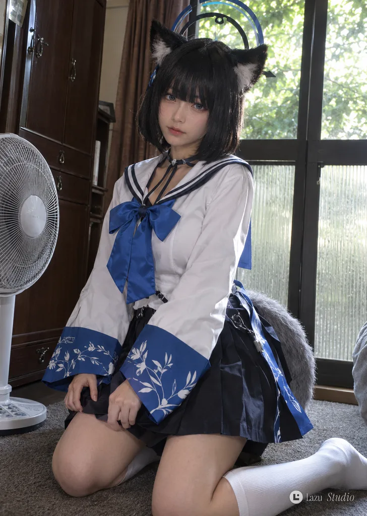 Cosplayer with black cat ears and sailor costume kneeling indoors on a gray carpet.