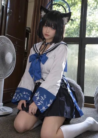 Cosplayer with black cat ears and sailor costume kneeling indoors on a gray carpet.