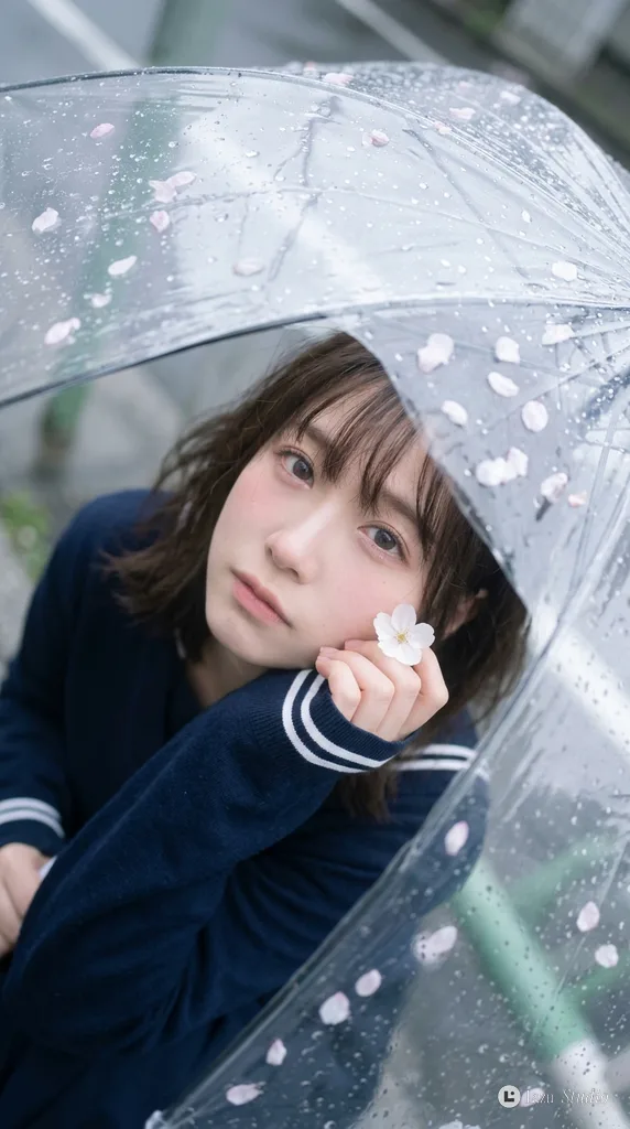 Top-down view of a young woman looking up through a wet, clear umbrella with rain droplets.