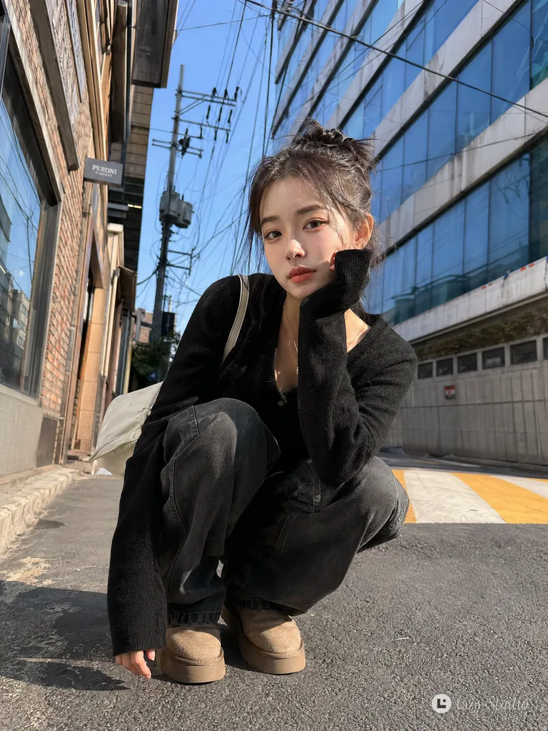 Low-angle shot of a stylish young Asian woman squatting outdoors on a sunny street pavement.