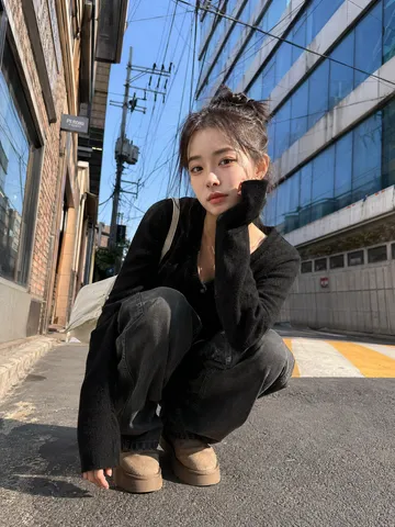 Low-angle shot of a stylish young Asian woman squatting outdoors on a sunny street pavement.