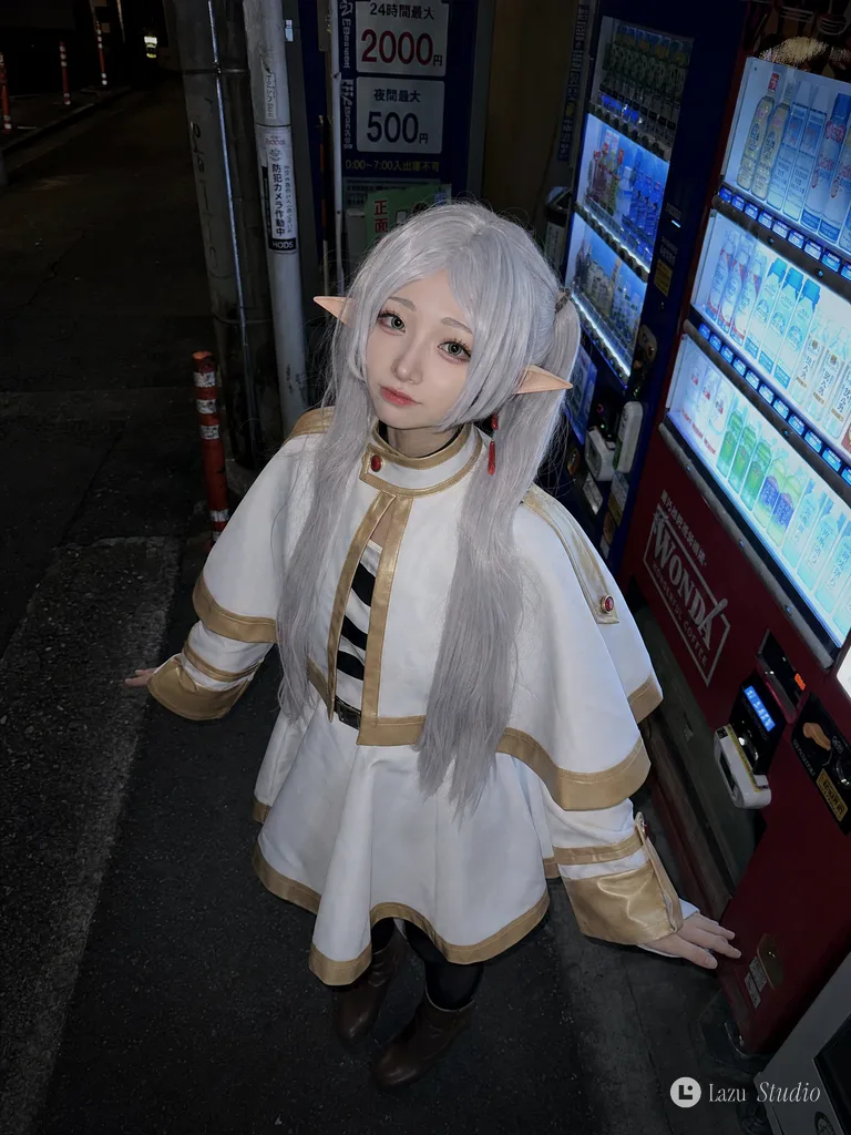 Woman in Frieren cosplay looking up at the camera beside illuminated vending machines at night.
