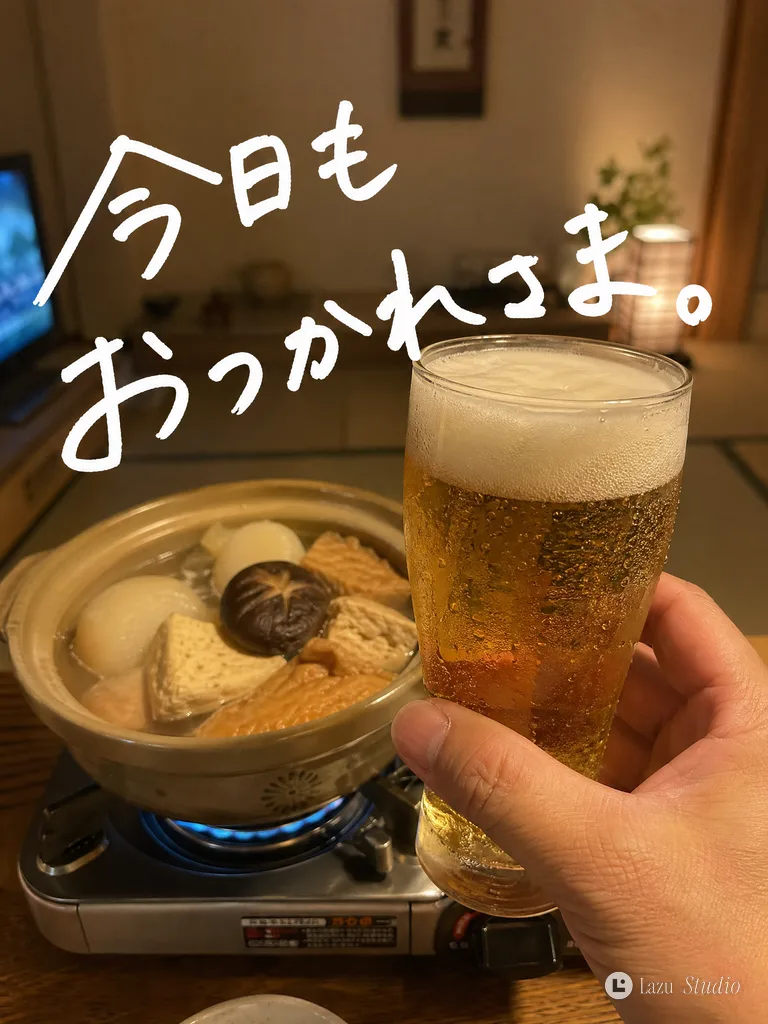 Hand raising a frothy glass of beer in front of a simmering pot of oden on a table.