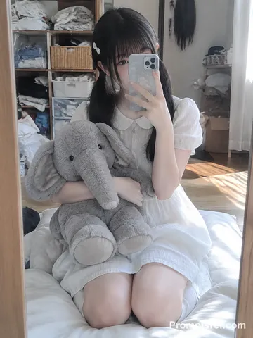 Mirror selfie of a woman kneeling with a large stuffed elephant covering part of her face.