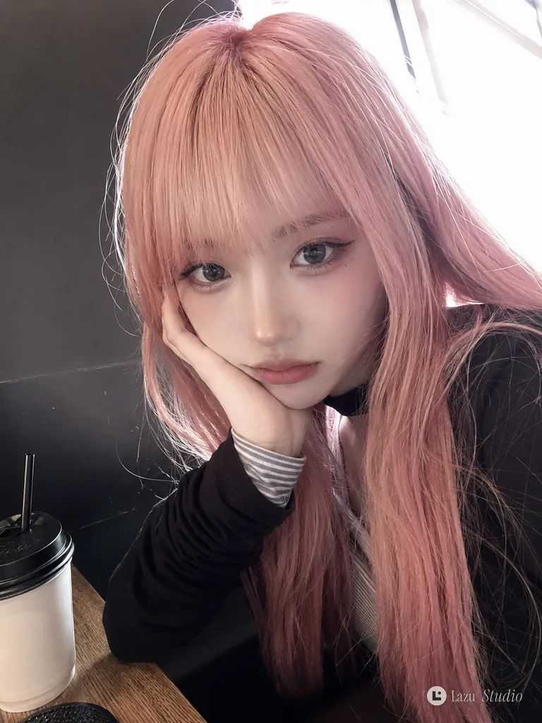 Close-up selfie of a young woman with pastel pink hair leaning her cheek on her hand in a café.