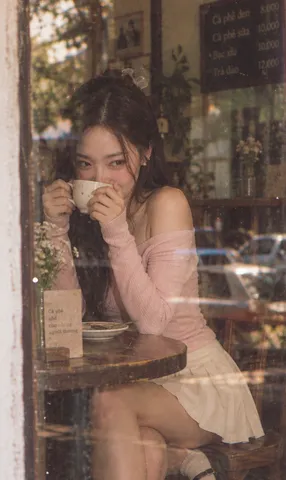 Vintage film portrait of a Vietnamese woman in an off-shoulder top smiling shyly in a café.
