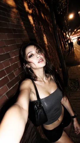 Low-angle flash selfie of a woman with wavy hair on an amber-lit city street at night.