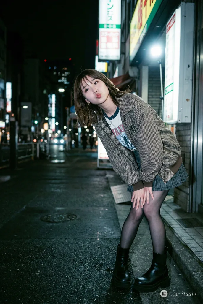 Off-center night street photo of a fashionable young woman illuminated by direct camera flash.