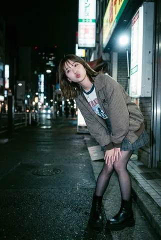 Off-center night street photo of a fashionable young woman illuminated by direct camera flash.