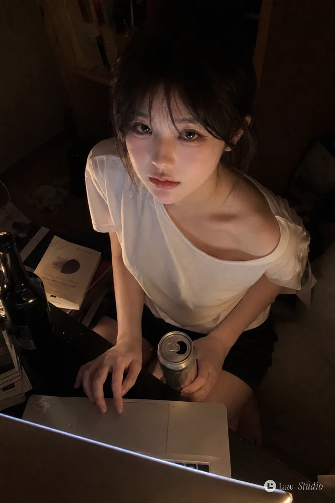 Overhead snapshot of a young woman sitting by a laptop in a dimly lit room, gazing upward.