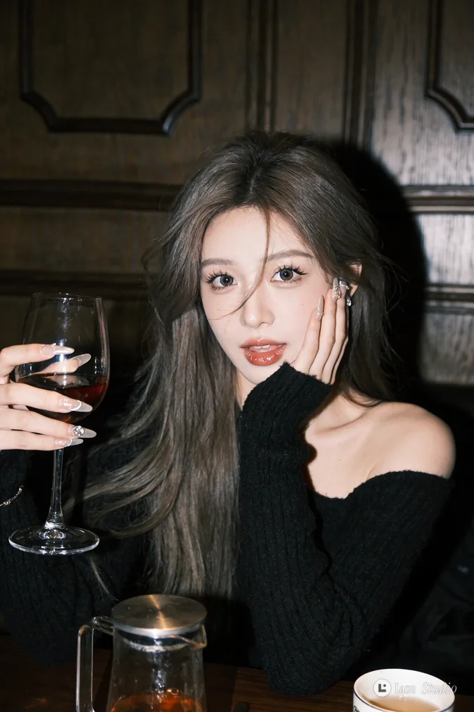 Young woman holding a wine glass and resting her cheek on her hand at a dark table.