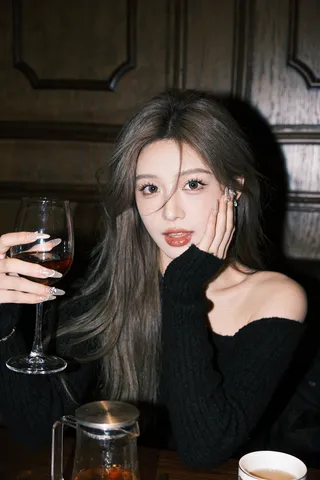 Young woman holding a wine glass and resting her cheek on her hand at a dark table.