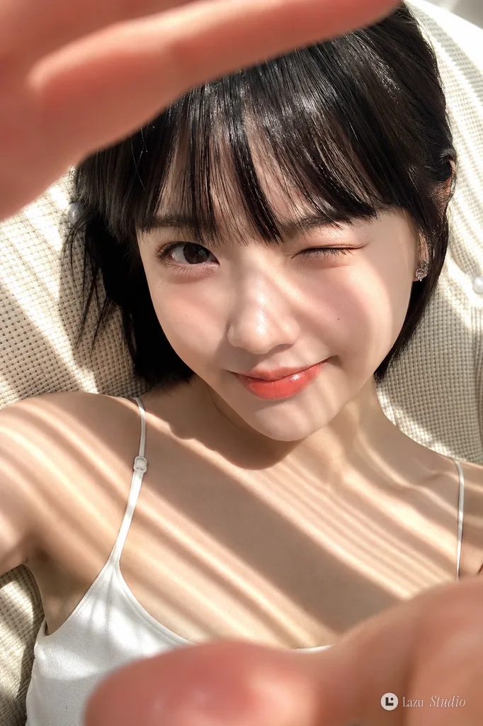 Close-up portrait of a smiling young woman with short black hair winking in bright sunlight.