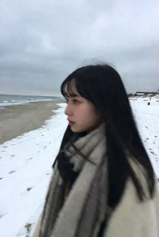 Side profile snapshot of a young Japanese woman in a coat walking along a quiet snowy beach in winter.