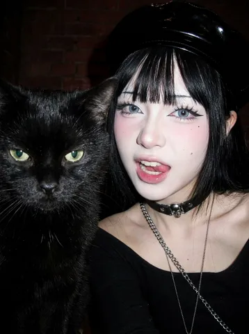 Direct-flash close-up selfie of a gothic-styled young woman posing alongside a cat.