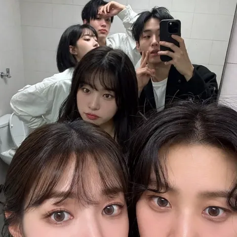 Candid mirror selfie of stylish young women in casual clothing inside a home bathroom.
