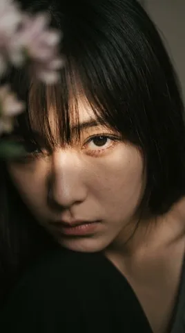 Extreme close-up of a person's face with dark bangs and one eye highlighted by warm directional light.