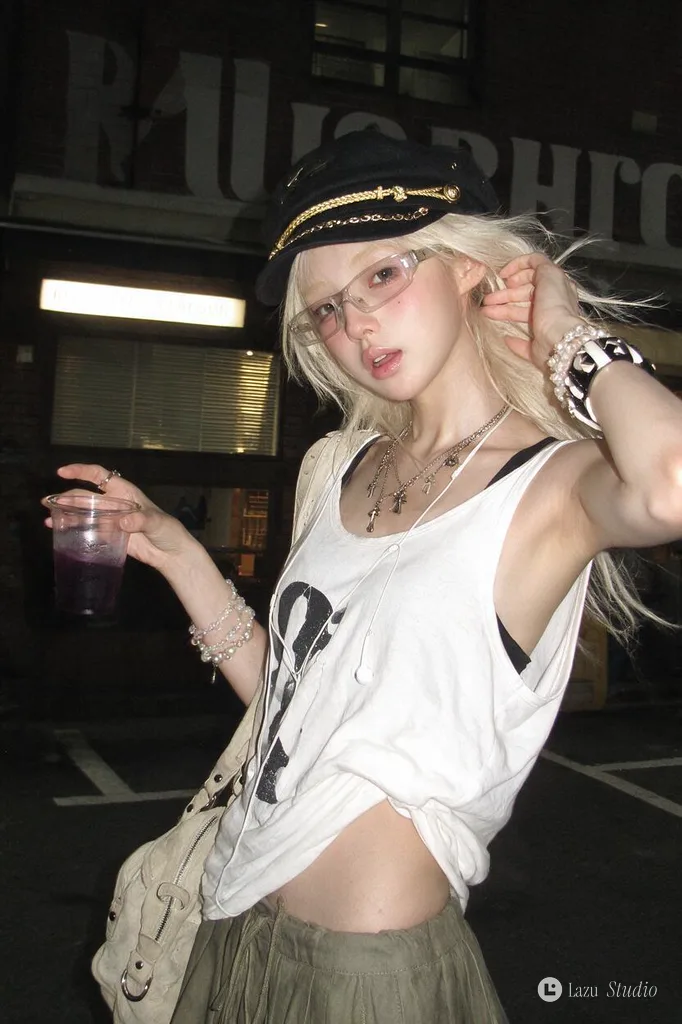 Young woman with platinum hair and black cap holding a purple drink outside a brick storefront at night.