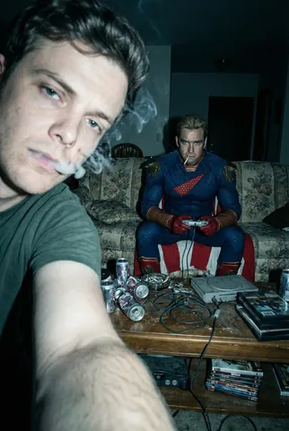 A gritty direct-flash photo of Hughie smoking close to the camera while Homelander plays games on a couch.