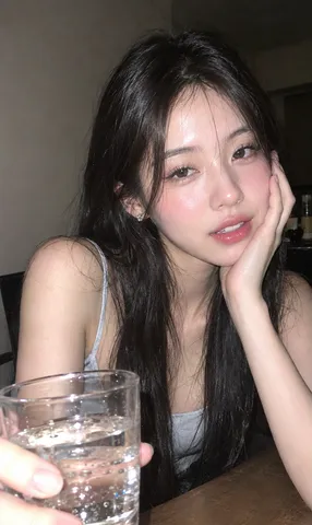 Woman resting her cheek on her hand, holding a clear glass under direct camera flash.